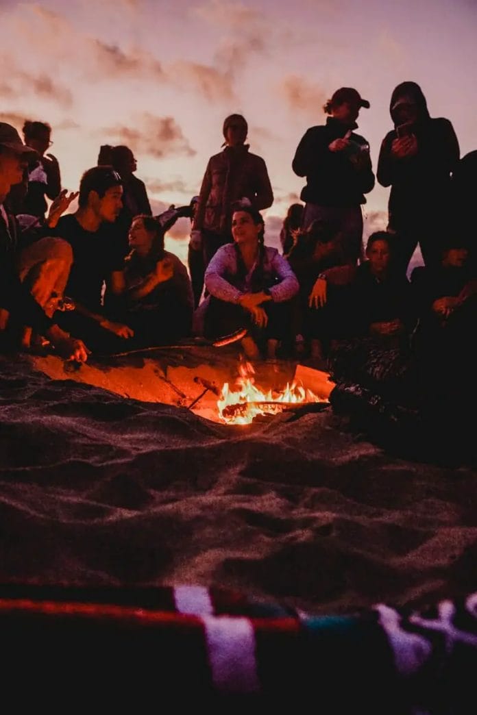 people sitting on brown sand near bonfire during night time